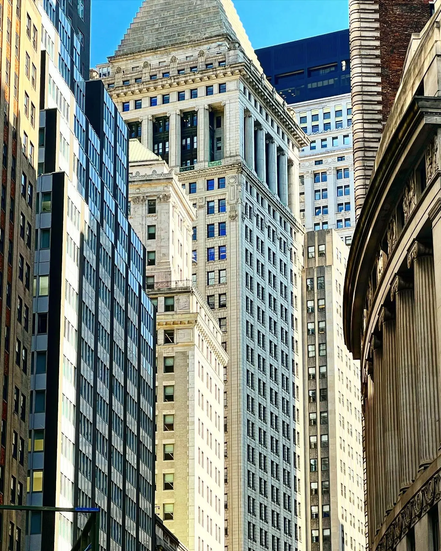 Downtown Manhattan office towers stacked against each other, looking up from the street on a bright day