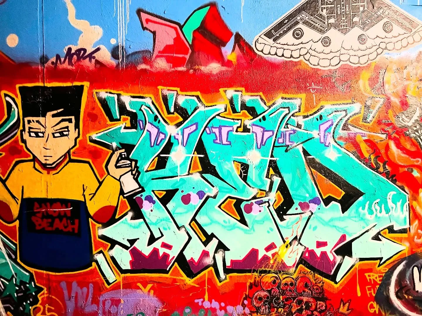 A full graffiti wall in turquoise, red and orange, with a cartoon figure holding a spray can at the left