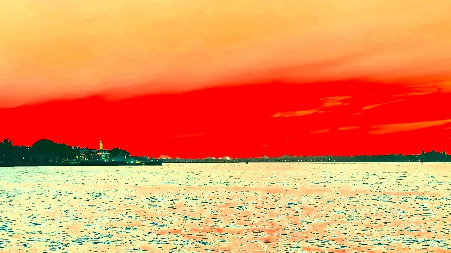 New York Harbor under a deep red sunset, with the Statue of Liberty a small silhouette on the far shore