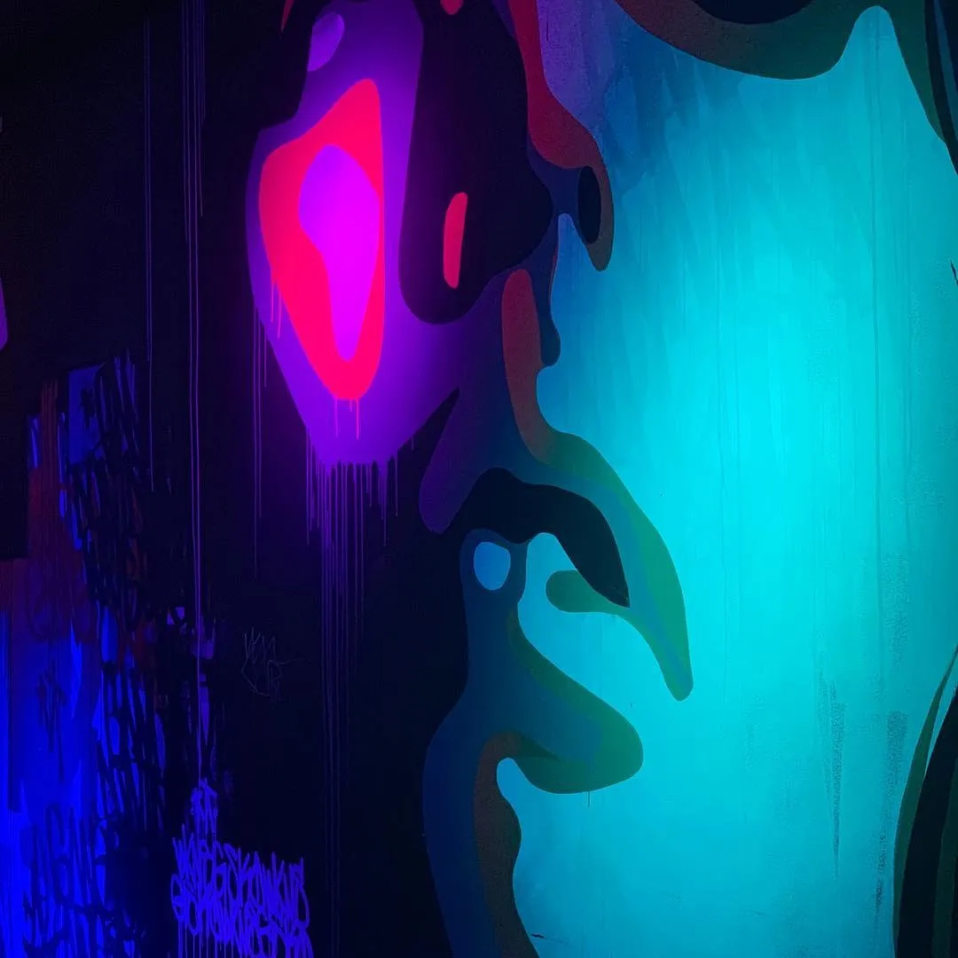 A mural lit in the dark, an electric cyan face against magenta and purple