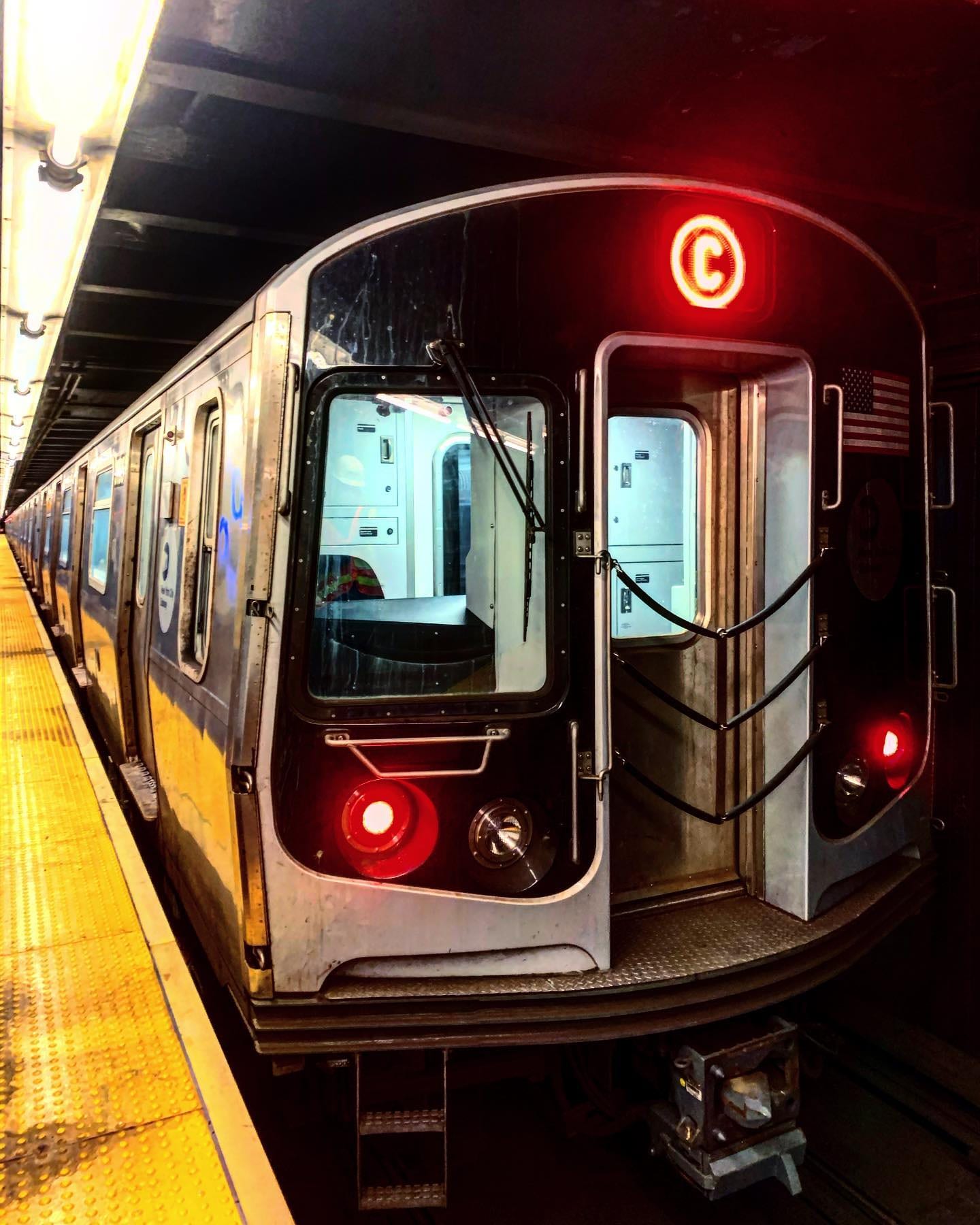 A C train pulling into the platform with its headlights on.
