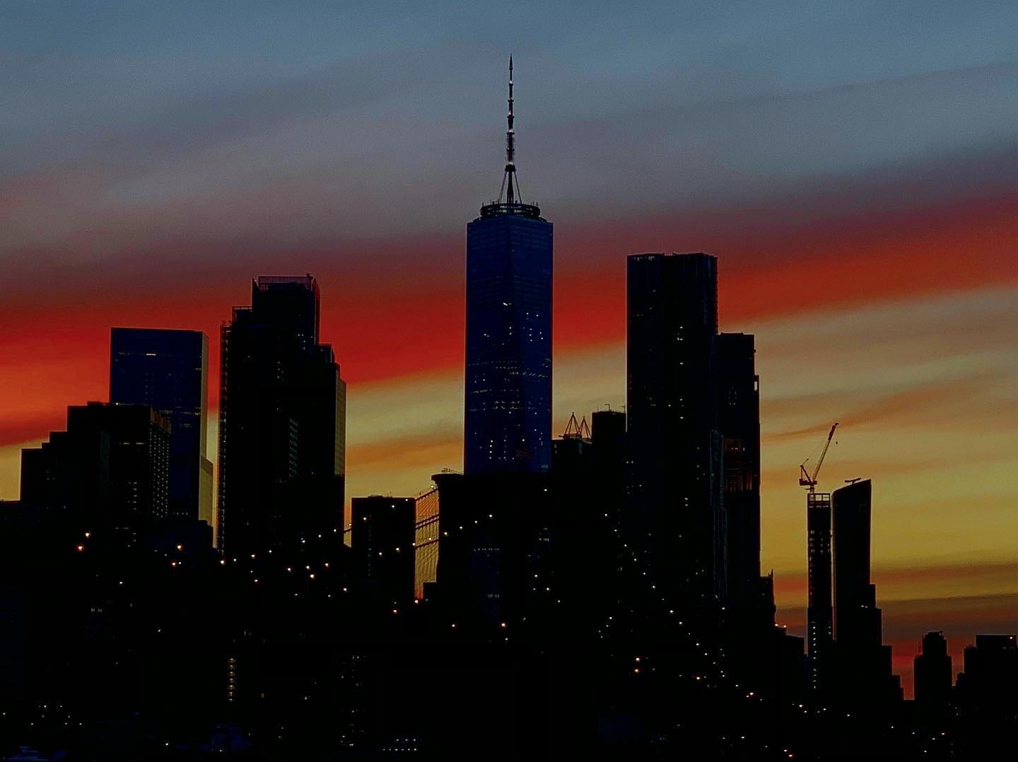 The Lower Manhattan skyline in silhouette against a red and orange sunset.