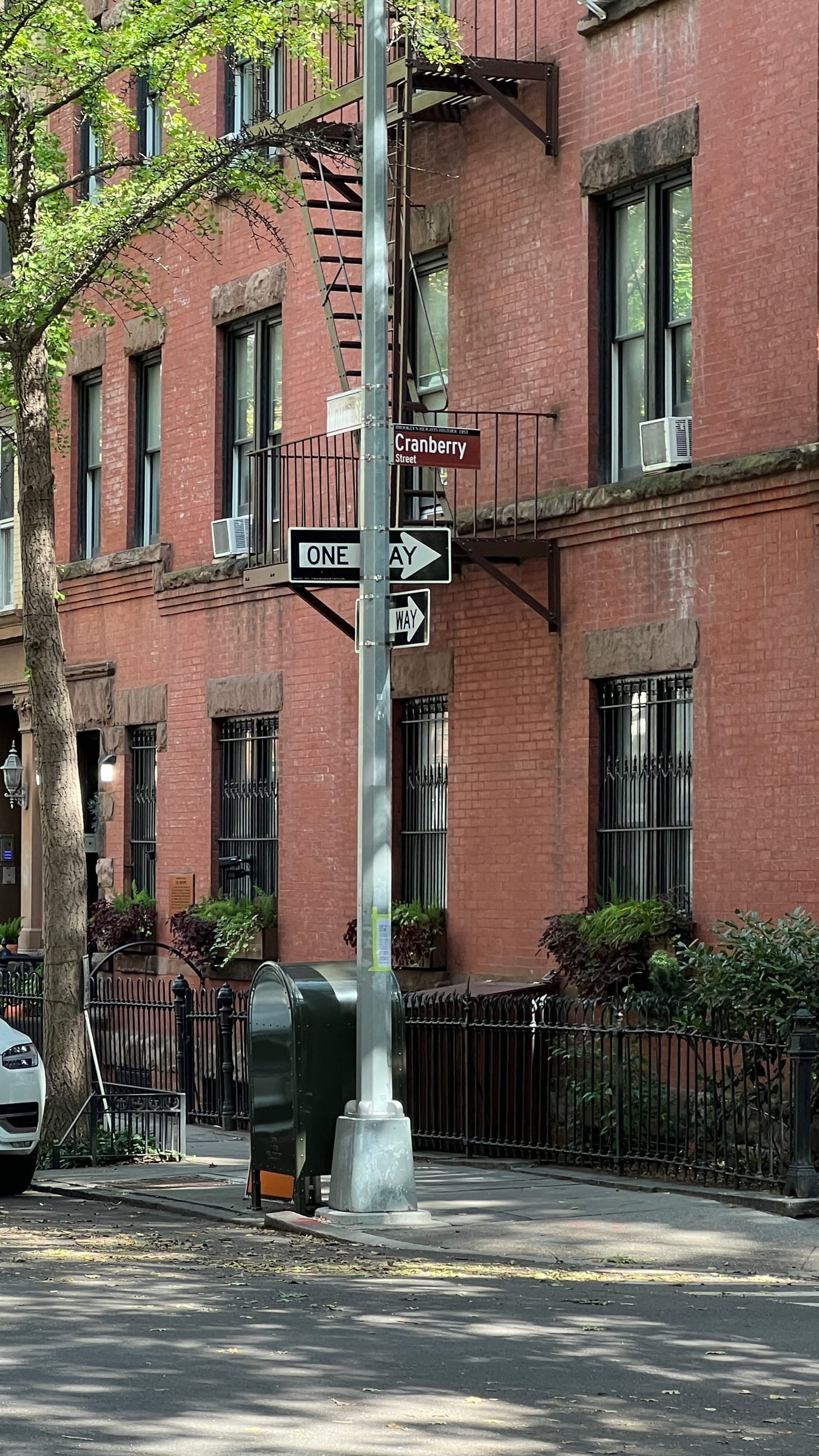 A red-brick building with a fire escape on Cranberry Street in Brooklyn Heights, in afternoon sun.