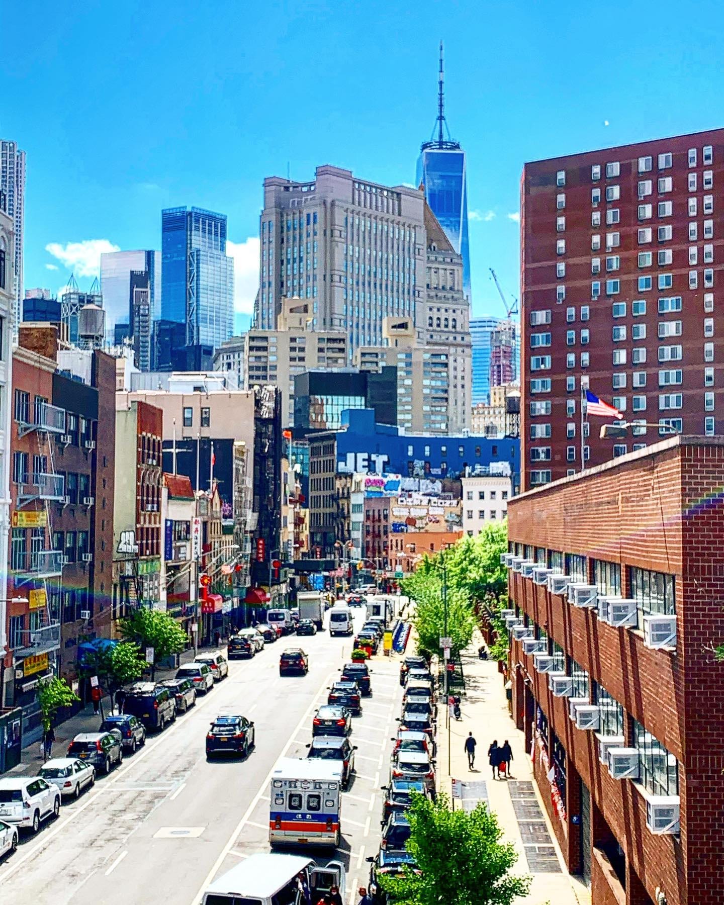 Chinatown seen from above: a busy street lined with Chinese shop signs, running toward the Lower Manhattan towers and One World Trade Center.