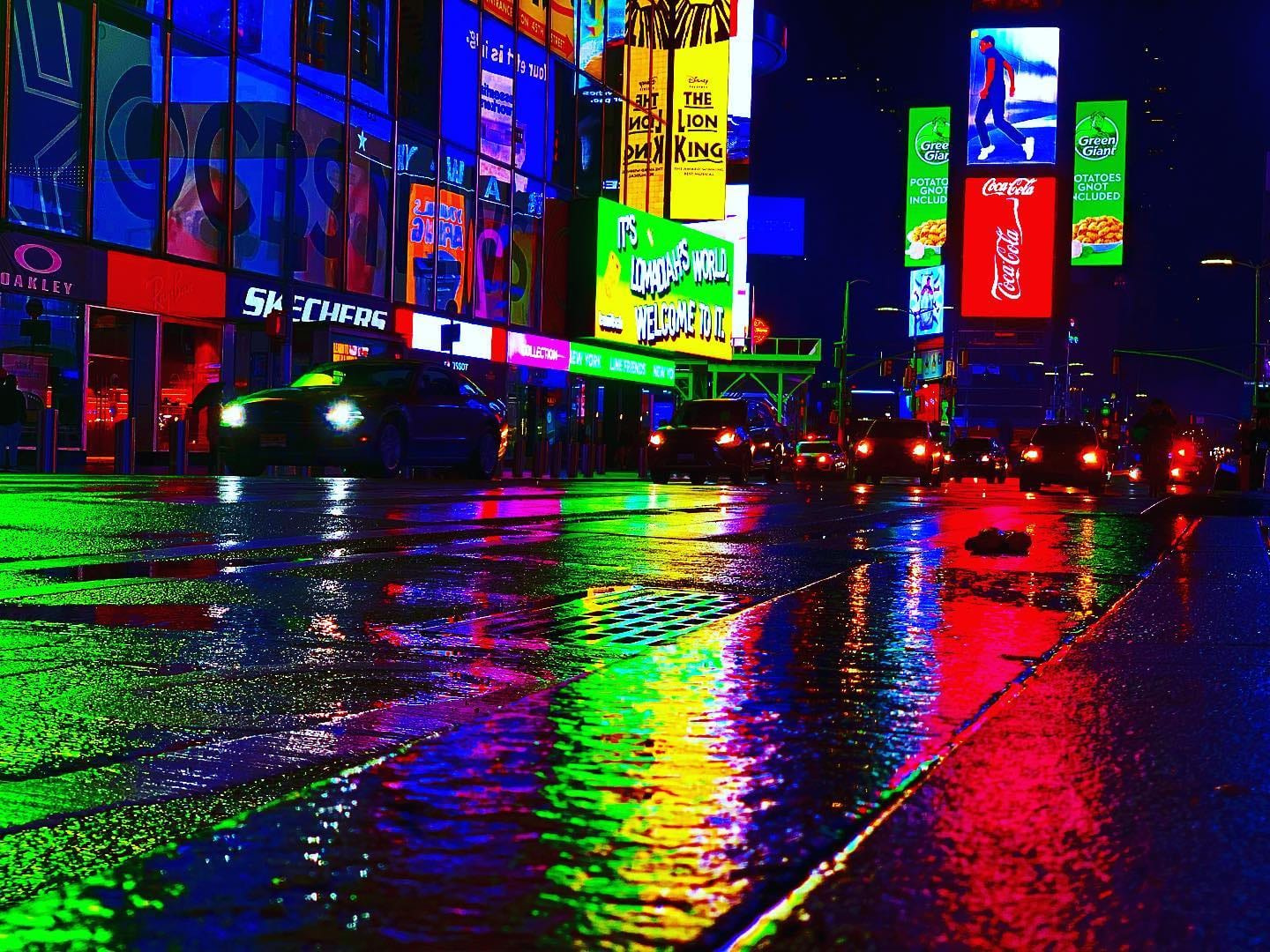 Times Square at night in the rain, its neon signs smeared in reflections across the wet street.