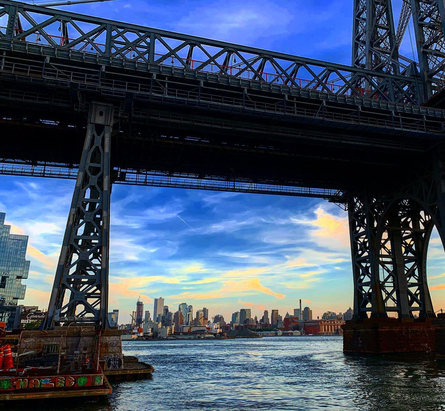The Williamsburg Bridge framing the Manhattan skyline across the East River at golden hour.